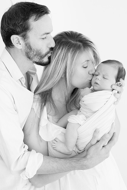 Black and white parents kissing their newborn